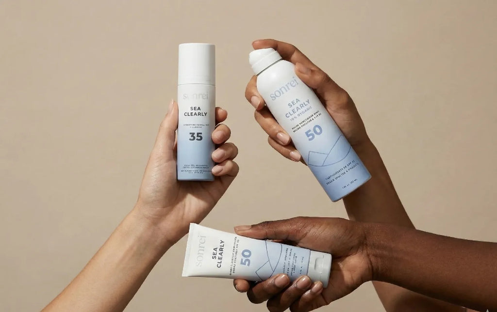 Three hands holding sunscreen products against a beige background